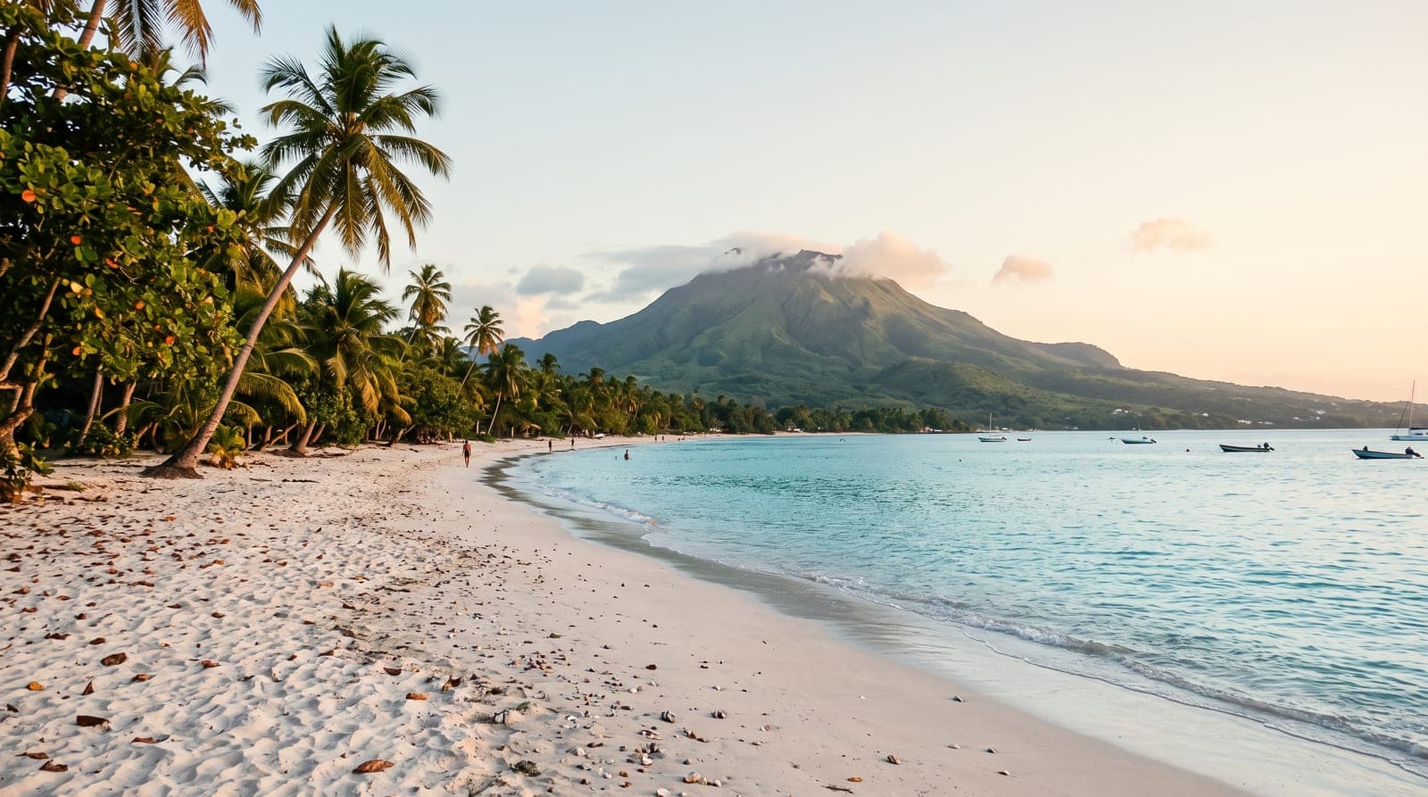 Heller Sandstrand mit Kokospalmen auf Guadeloupe, türkisfarbenes Meer und grüner Vulkan am Horizont