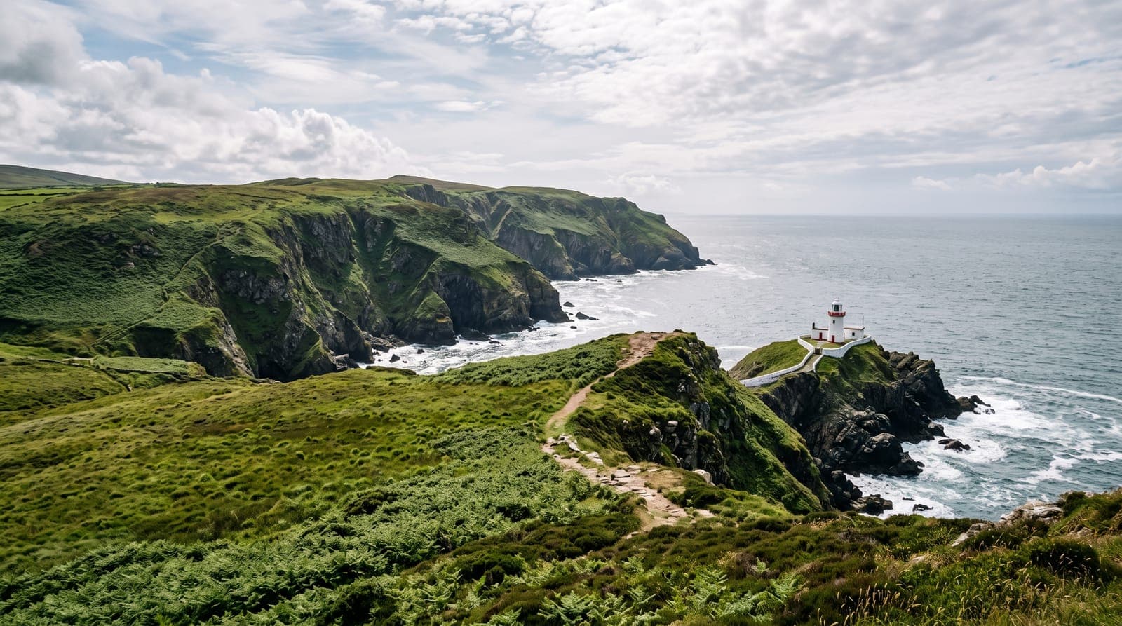 Küste der Isle of Man mit grünen Klippen, einem Kammweg und einem kleinen Leuchtturm an der Irischen See