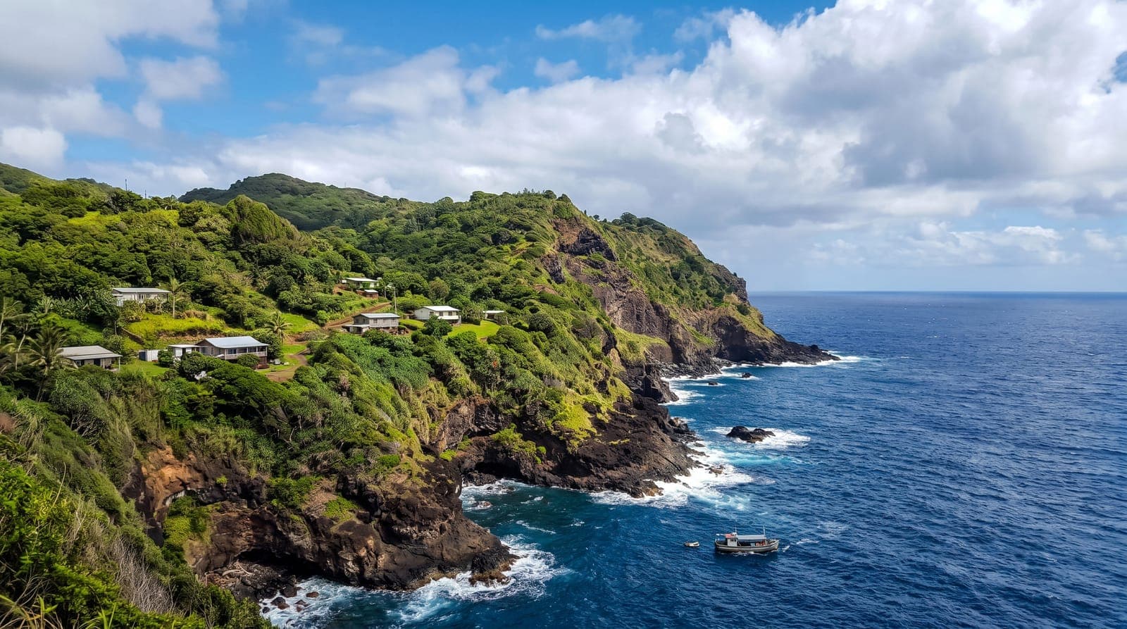 Steile, grüne Küste der Insel Pitcairn, einzelne Häuser und ein vor Anker liegendes Boot