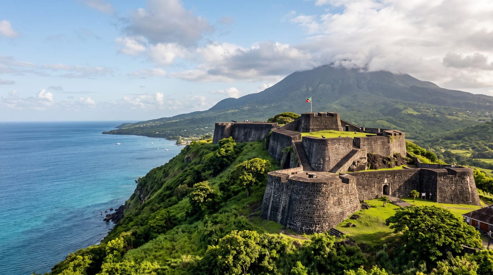 Festung Brimstone Hill auf St. Kitts, Wälle aus Vulkangestein auf einem grünen Hügel vor dem Karibischen Meer und einem bewaldeten Vulkan