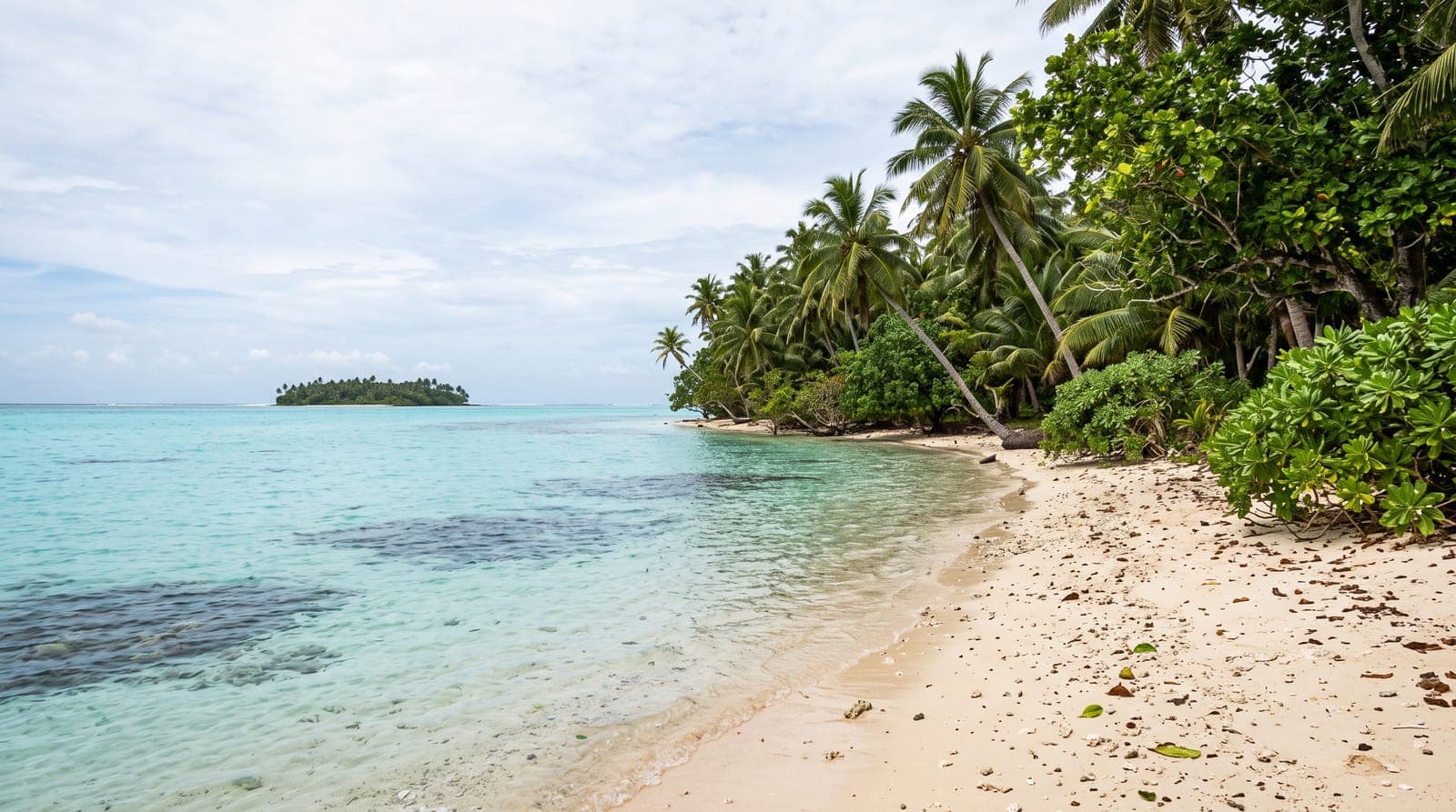 Lagune der Insel Wallis, ruhiges türkisfarbenes Wasser, ein heller Sandstrand mit Kokospalmen und ein kleines Inselchen in der Ferne